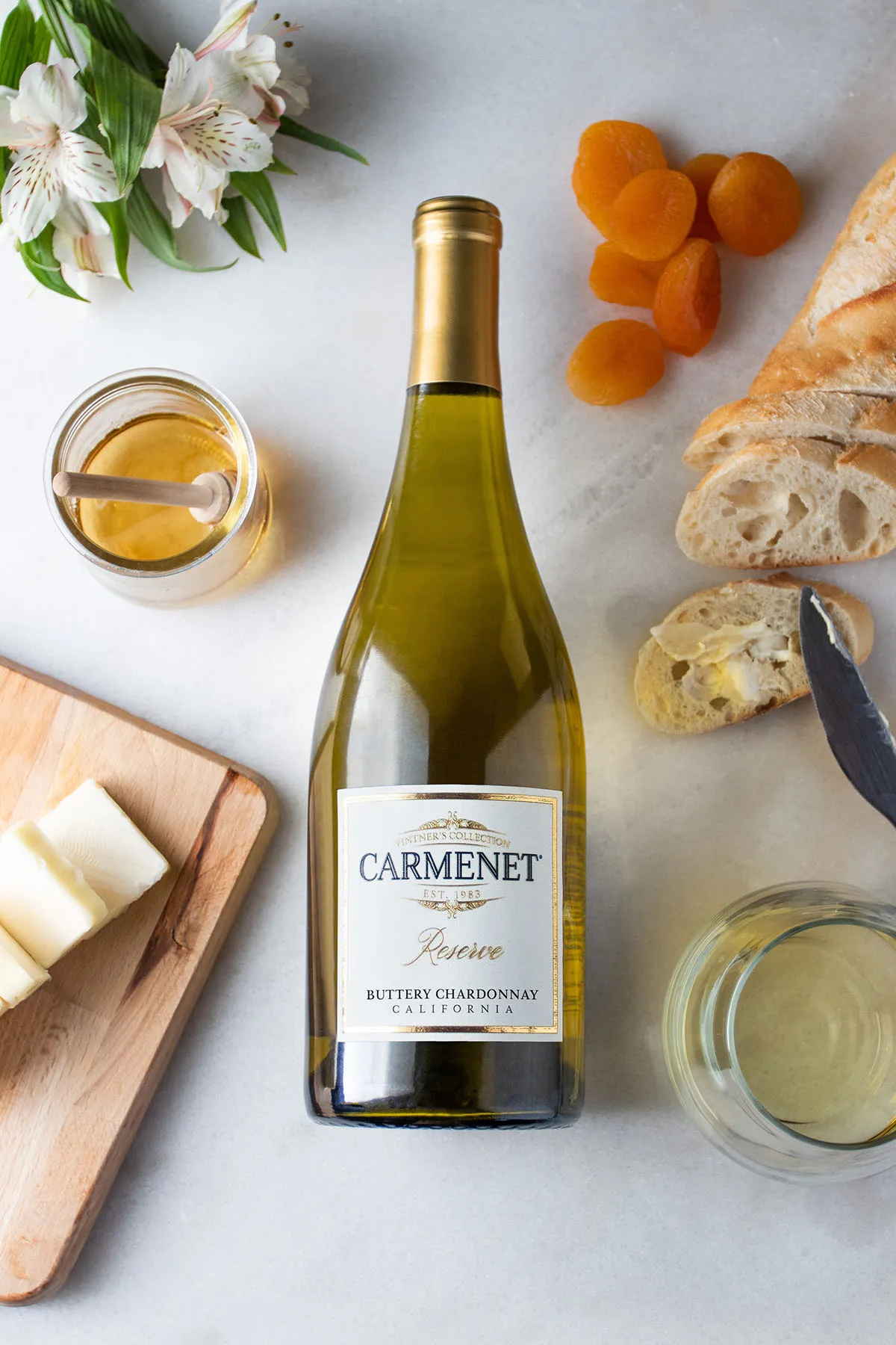 A bottle of Carmenet Buttery Chardonnay on a marble background with bread, cheese and honey