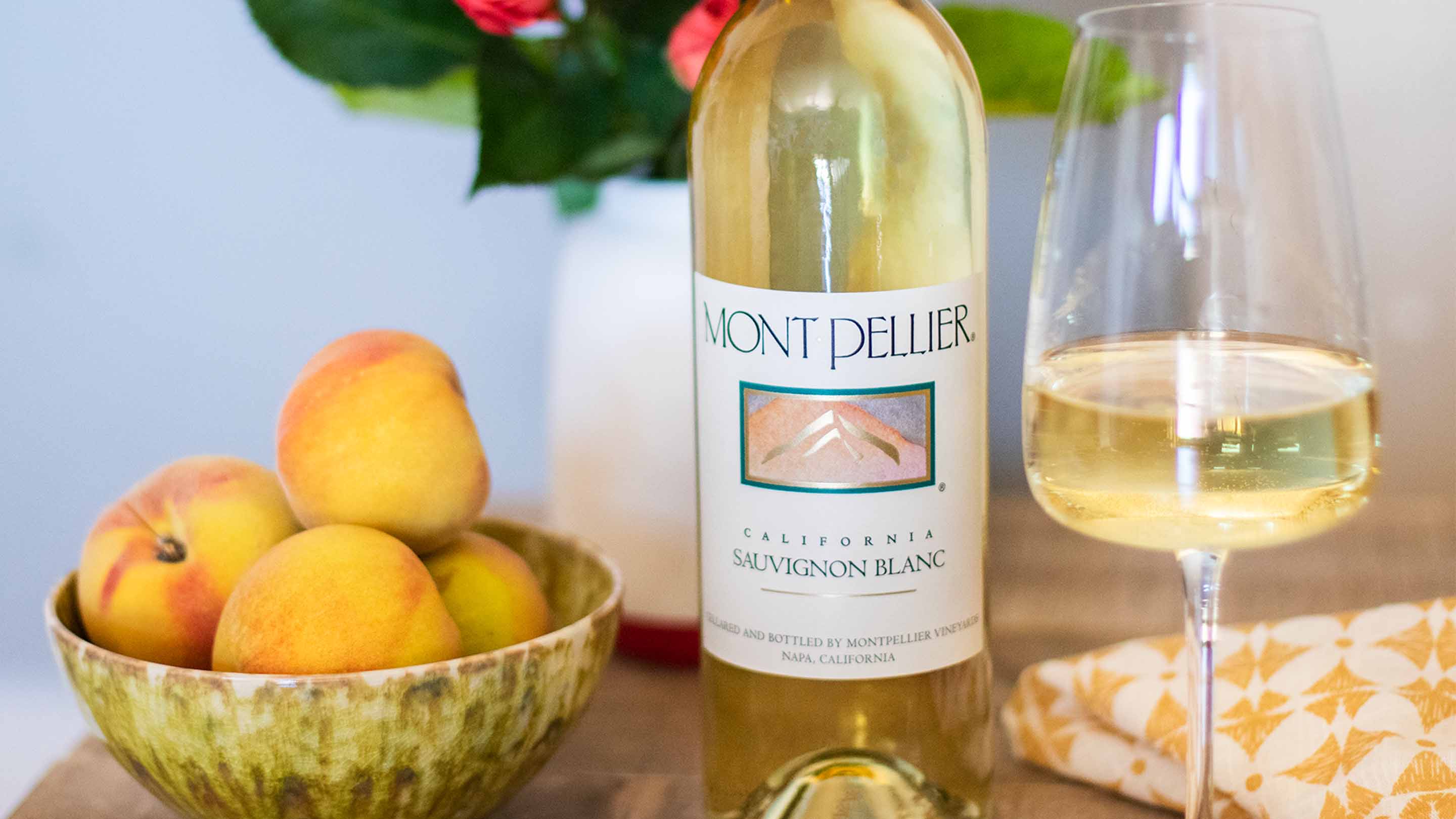 A bottle and glass of Montpellier Sauvignon Blanc on a table next to a bowl of peaches