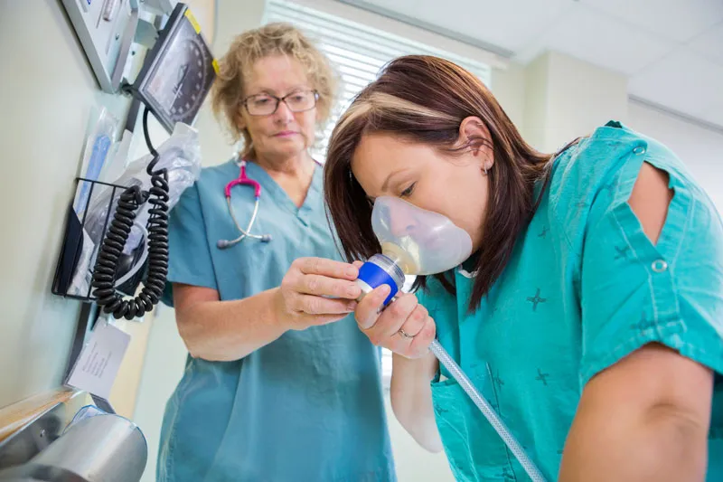 A patient inhaling laughing gas while the dentist is assisting her.