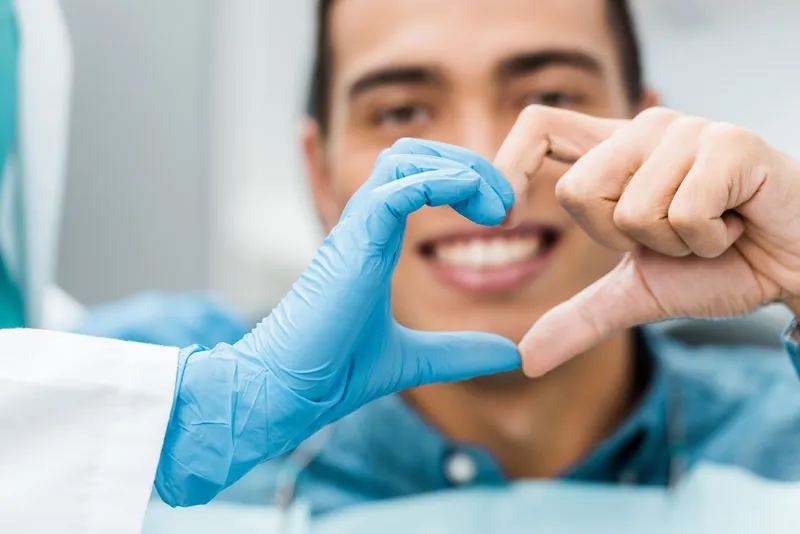 A dentist and a patient making a heart shape whit their fingers.