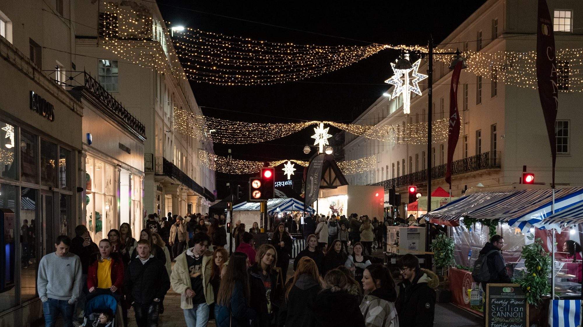Lots of pedestrians at a busy Christmas market with festive lights overhead