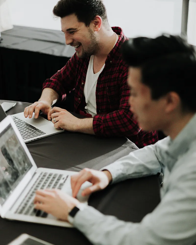 Zwei Männer sitzem mit Laptops an einem Schreibtisch.