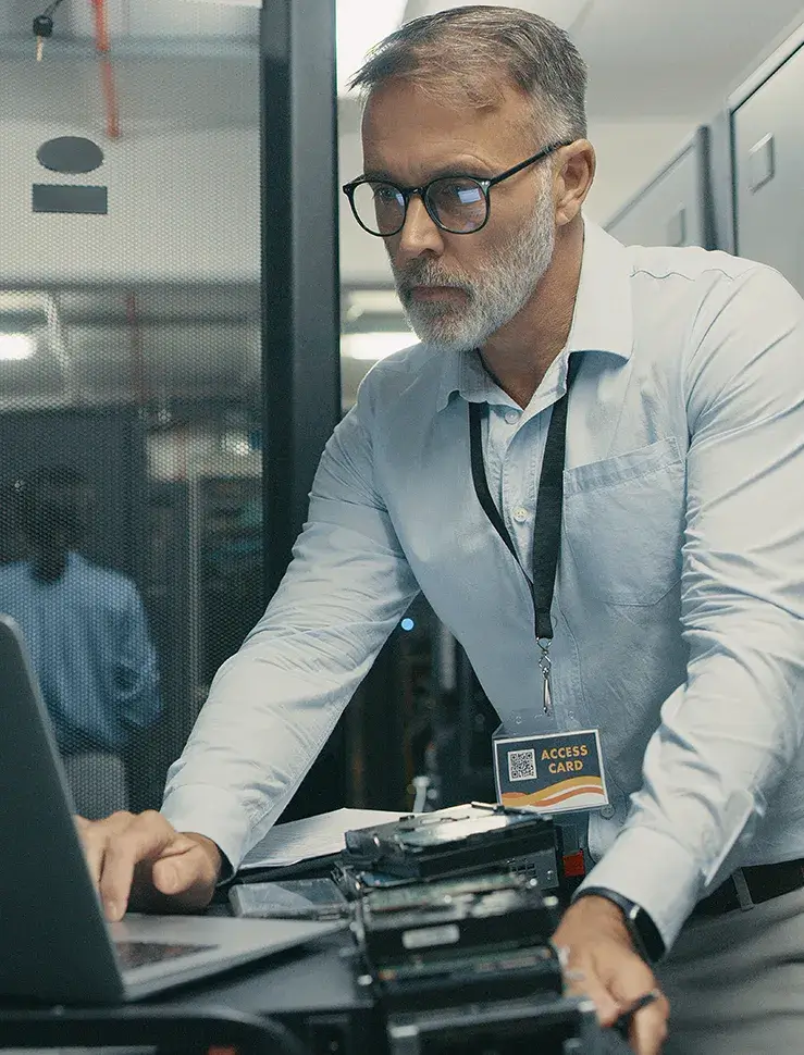 Ein IT Techniker ist im Rechenzentrum über einen Laptop gebeugt.