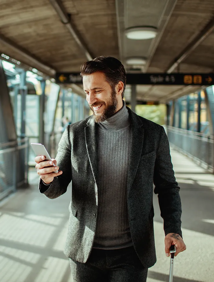 Geschäftsmann mit Smartphone in der Hand und Kabinentrolley am Bahnhof.