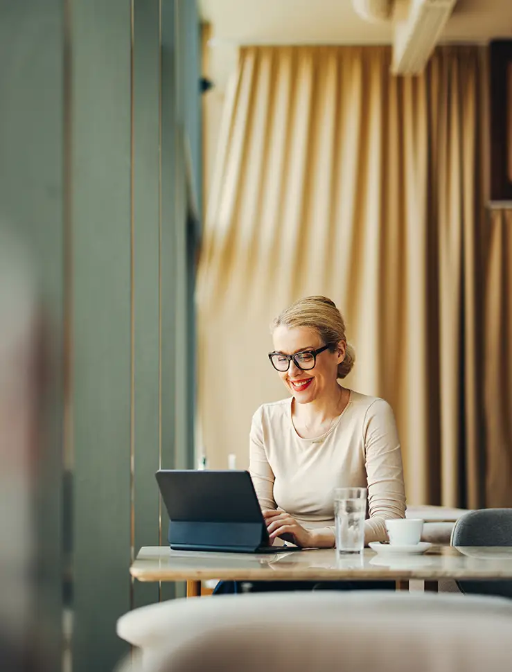 Eine Geschäftsfrau mit Brille sitzt am Tisch und schaut auf ihren Laptop