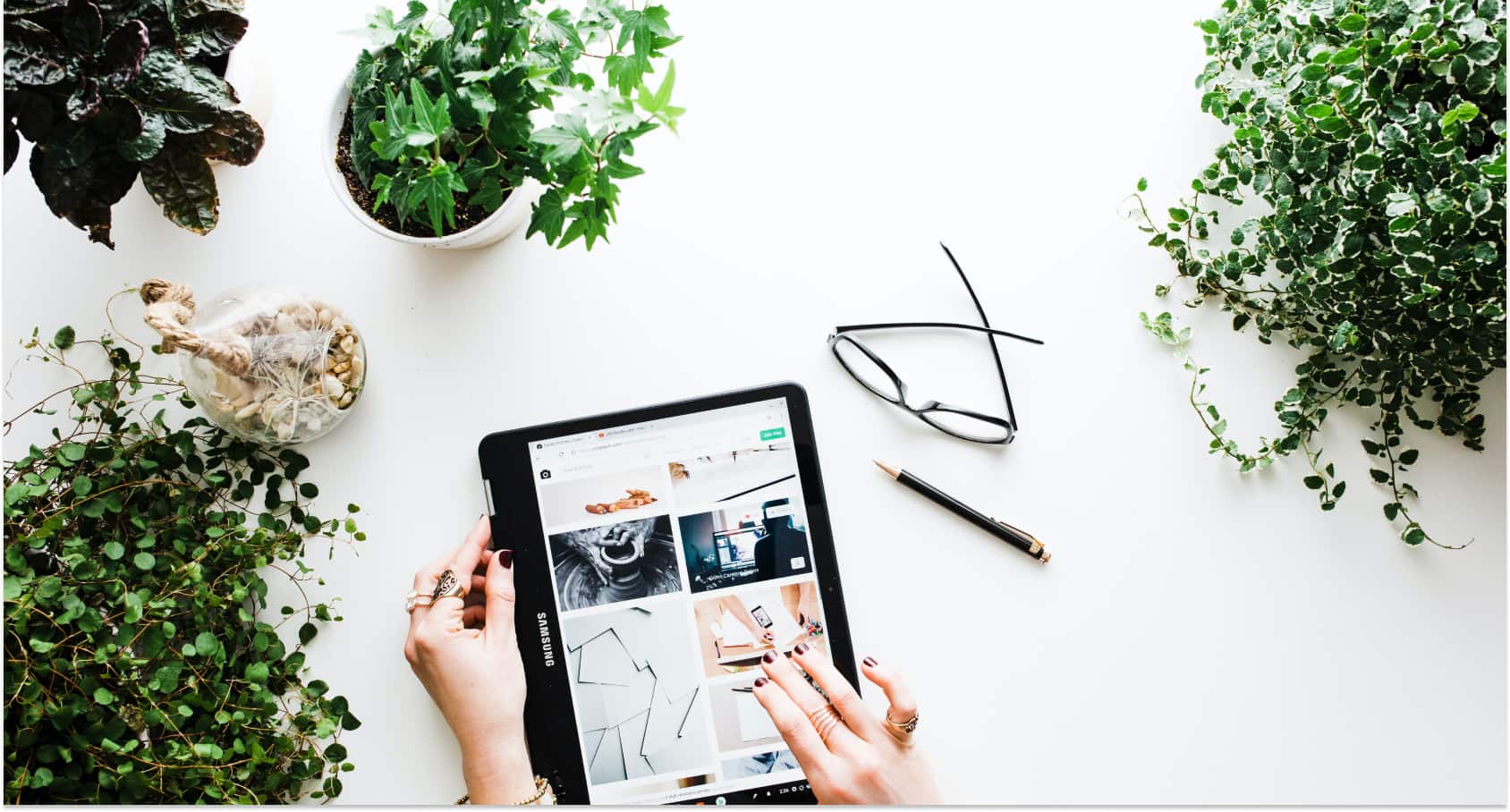 ipad showing images on a desk with glasses and plants