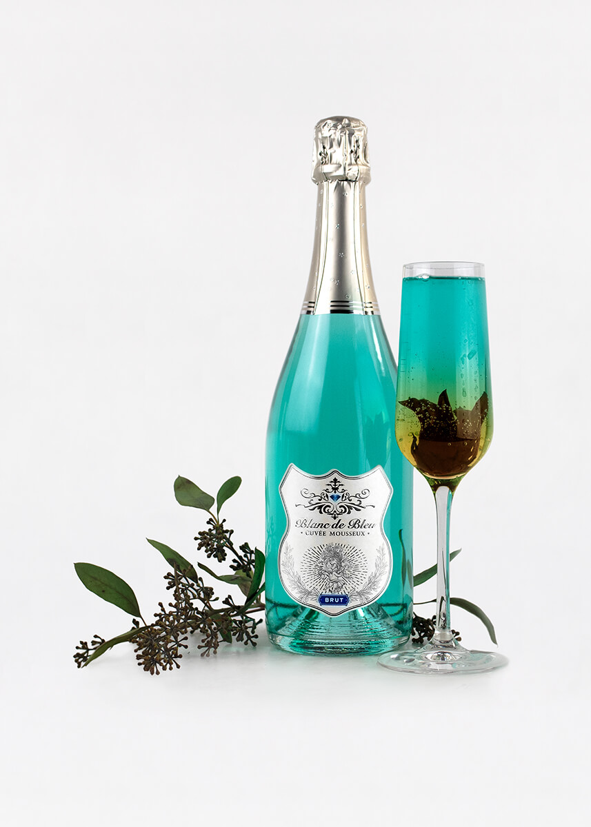 A "Lucky Flower" cocktail next to a bottle of Blanc de Bleu Brut and elderflower sprigs.