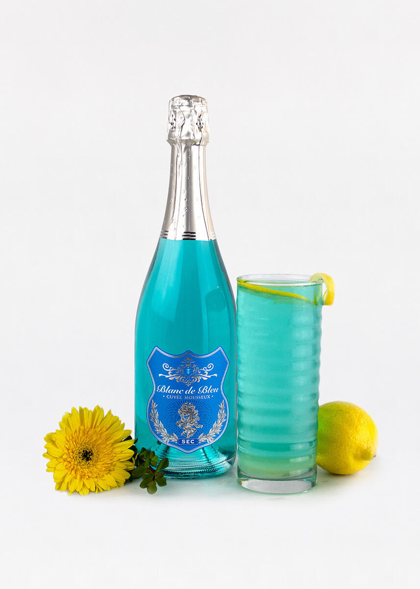 A "Bleu 75" cocktail next to a bottle of Blanc de Bleu Sec and sunflowers.