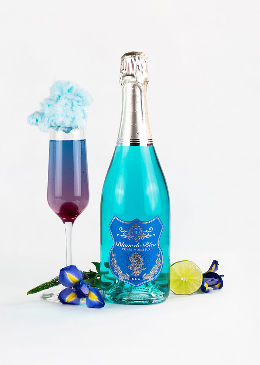 A "Cloud 9" cocktail next to a bottle of Blanc de Bleu Sec, a lime, and a flower.