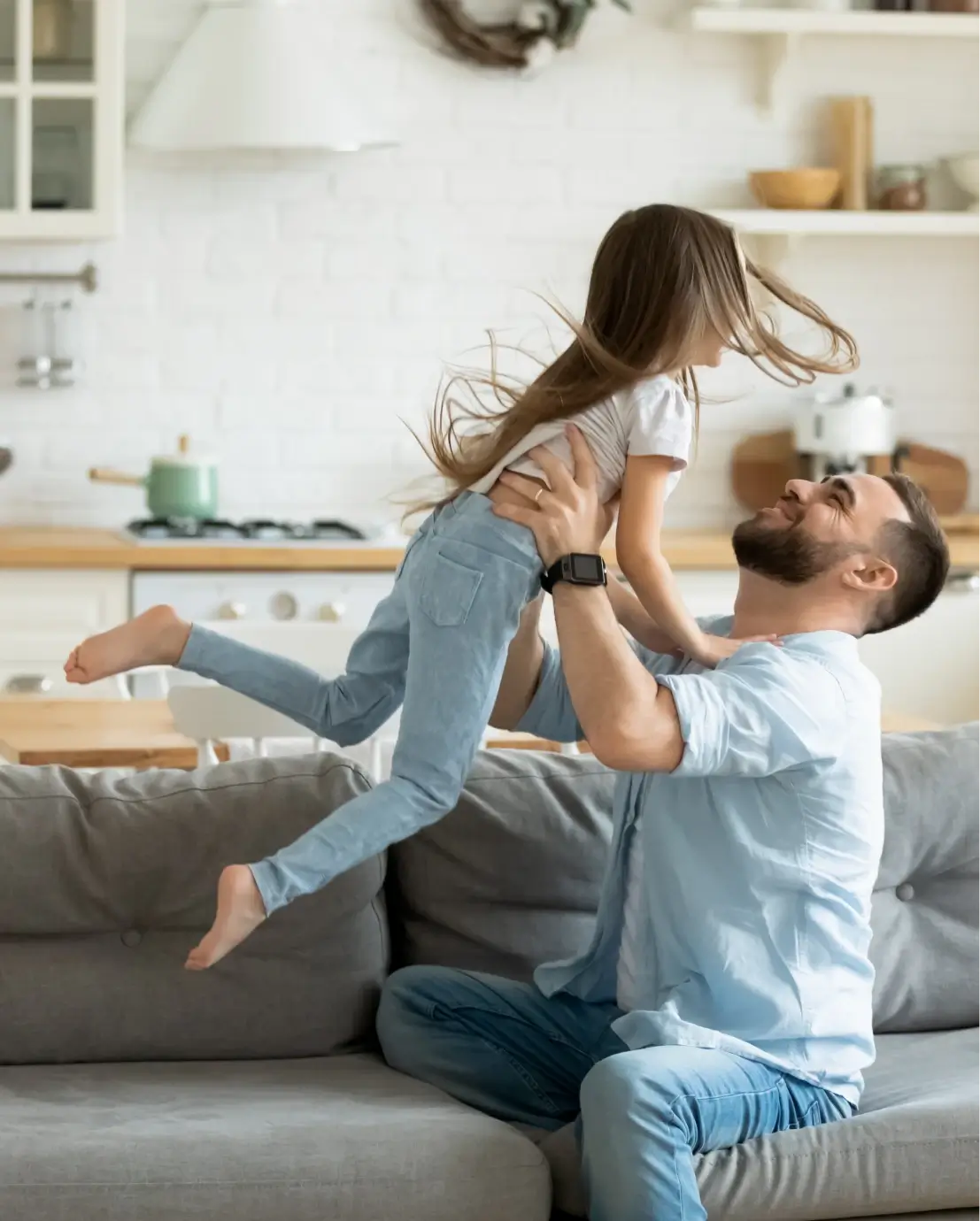 Adorable Vorschultochter fliegt mit ausgestreckten Händen in fürsorglichen Vater Armen in der modernen Küche.