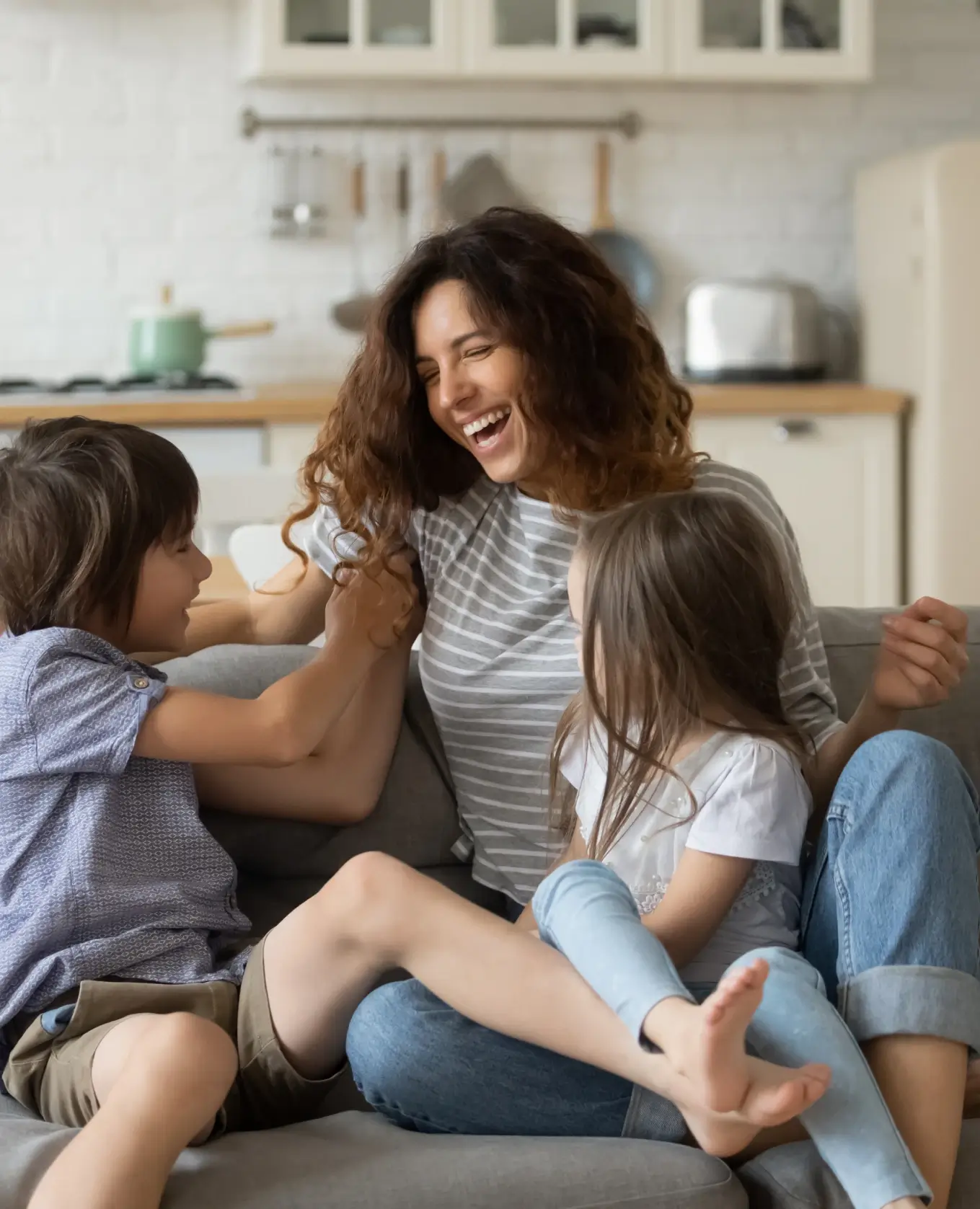 Überglückliche junge Mutter, die Spaß mit zwei Kindern zu Hause hat, bezaubernde kleine Tochter und Sohn spielen lustiges aktives Spiel, kitzeln, sitzen auf gemütlicher Couch im Wohnzimmer