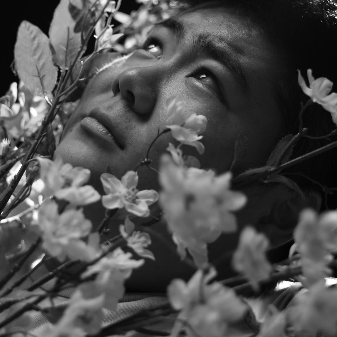 Black and white image of a man's face looking upwards surrounded by flowers