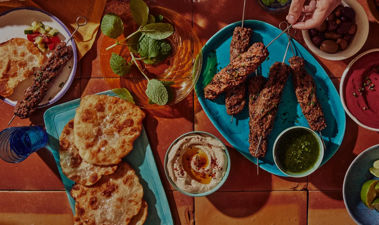 a plate of cultivated meat skewers part of a full meal with flatbread, olives and hummus