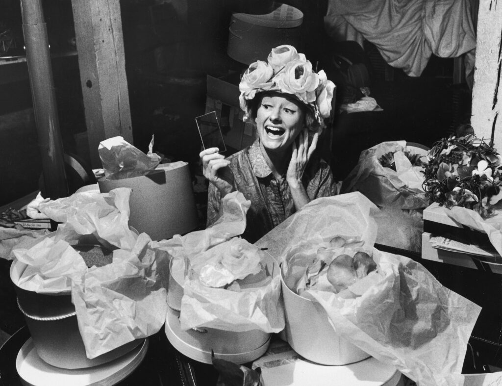 Phyllis Diller trying on hats with lots of boxes around her.