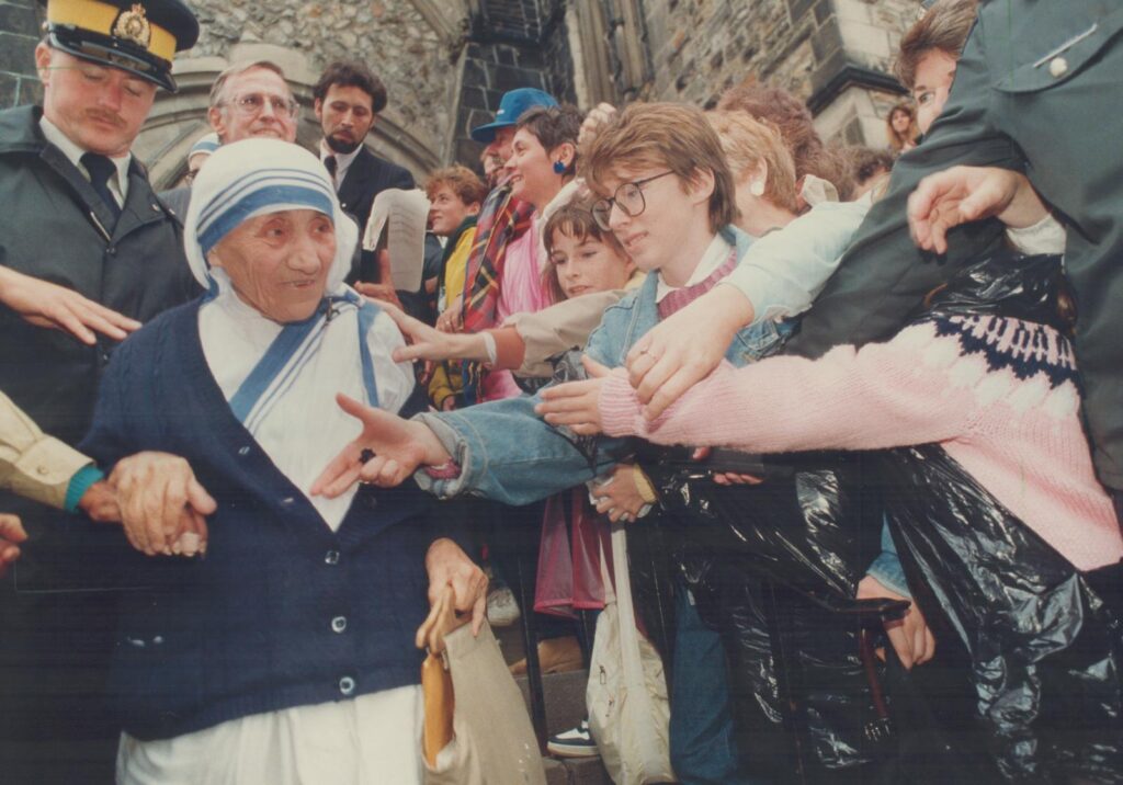 Mother Teresa walking by a crowd and shaking hands.